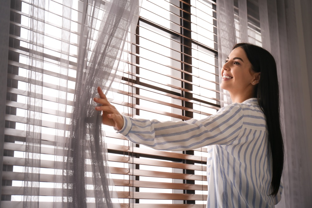 Woman opening sheer window treatments