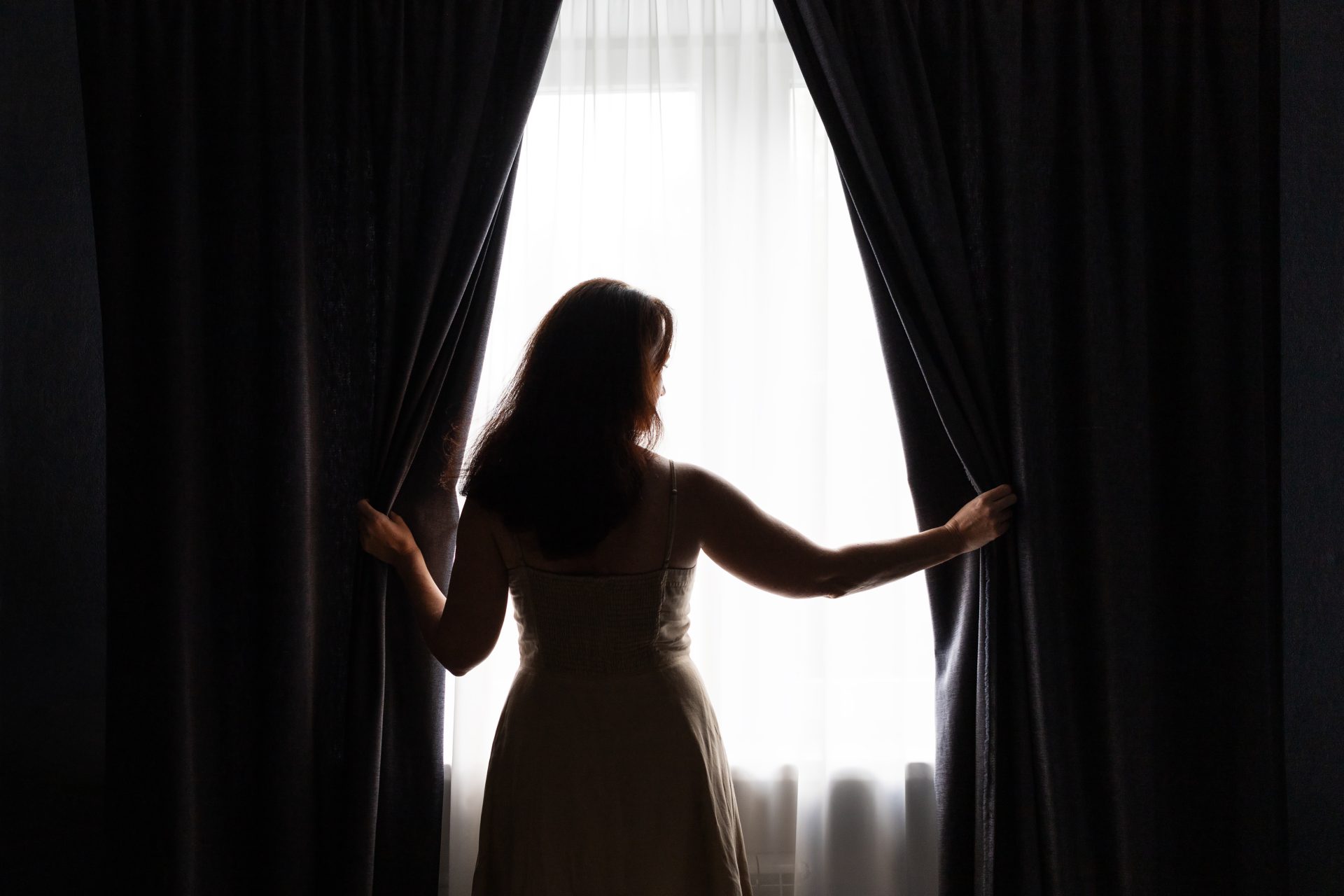 lady opening black out curtains on window 